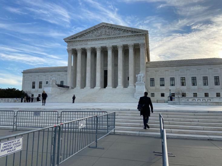 A man in a black suit walks up the stairs of the U.S. Supreme Court.