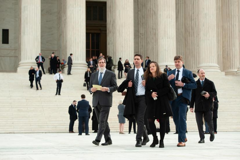 A group of attorneys and other people walk across the Supreme Court plaza.