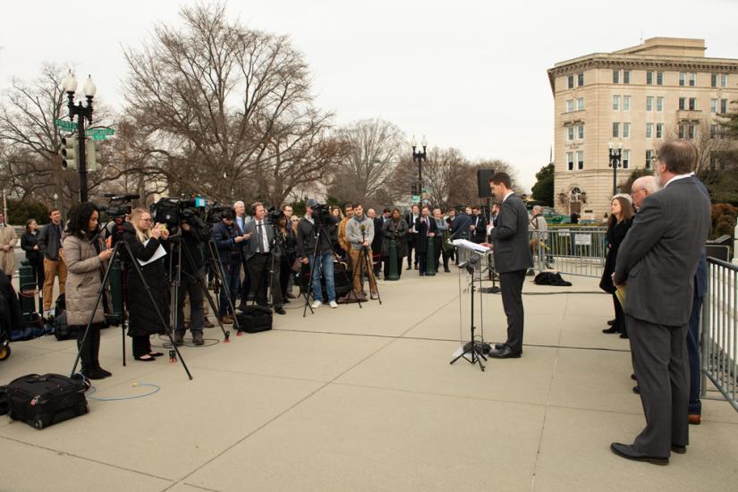 A slew of reporters and cameras are lined up across from a podium outside the Supreme Court.