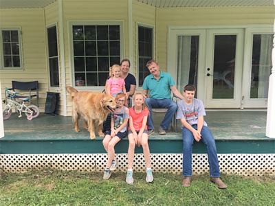 A family of two parents and four children sit on the back porch of their home with their golden retriever.
