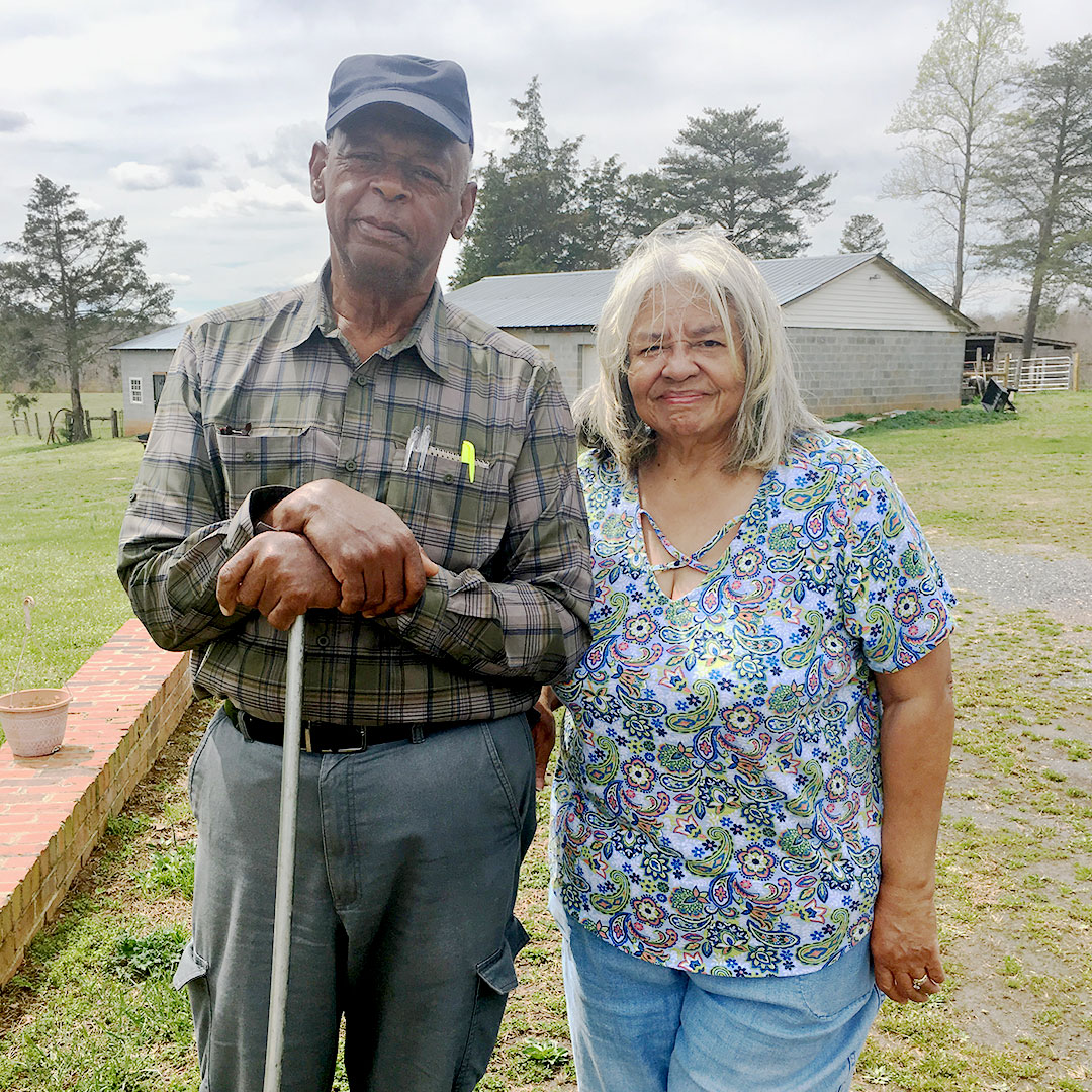 An elderly couple, John and Ruby Laury, smile in front of a farmhouse in Buckingham County.