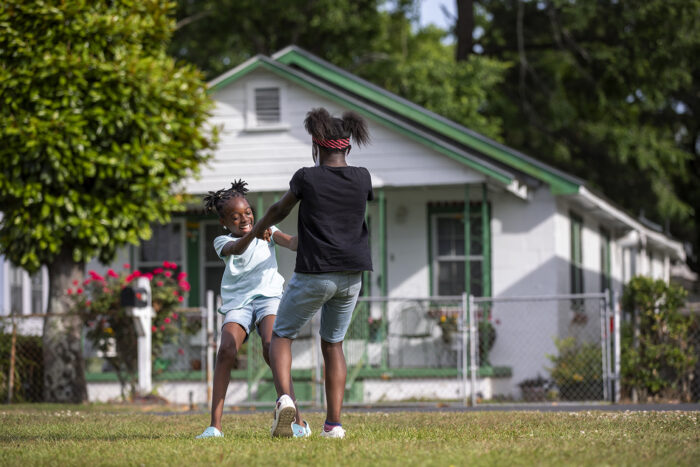Two young girls hold hands and spin around in a front yard in a Charleston neighborhood.