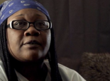 A woman in high contrast with oval glasses, braids, and a blue bandana speaks to the camera.