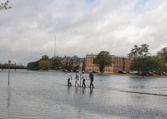Four students walk out single file on a flooded curb in Norfolk.