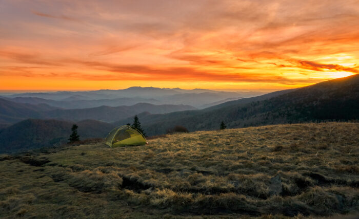 A tent is set up on the edge of field overlooking sunset in the Blue Ridge Mountains.
