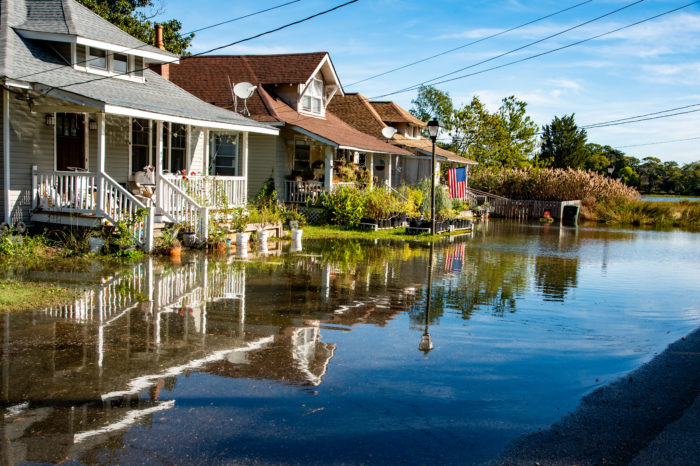 Two modest homes sit by side on a sunny day with the homes reflected in the flooded front yards.