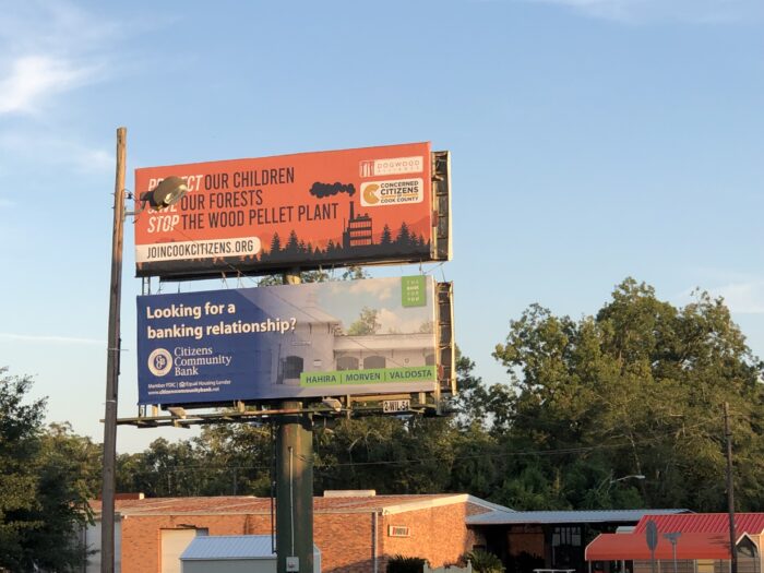 A billboard depicting a polluting biomass plant says Protect our children, save our forests, stpo the wood pellet plant.