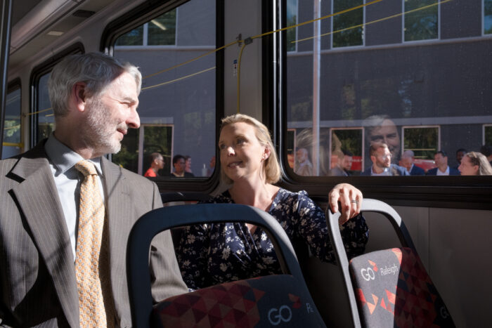 SELC attorneys David Neal and Kym Meyer look at each other while sitting together on an electric bus.