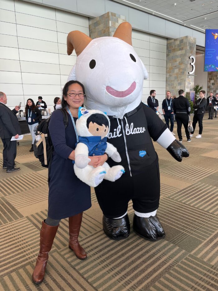 Donna, while hugging a large Salesforce-branded plushie, poses with Salesforce mascot Cloudy the Goat.