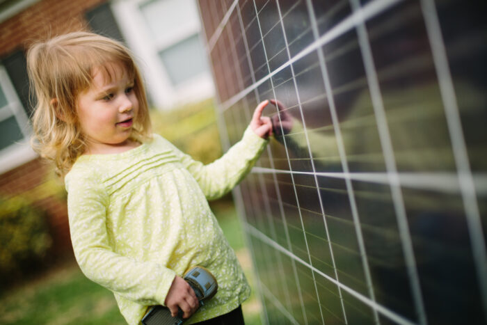 A young child curiously touches a solar panel in front of her home.